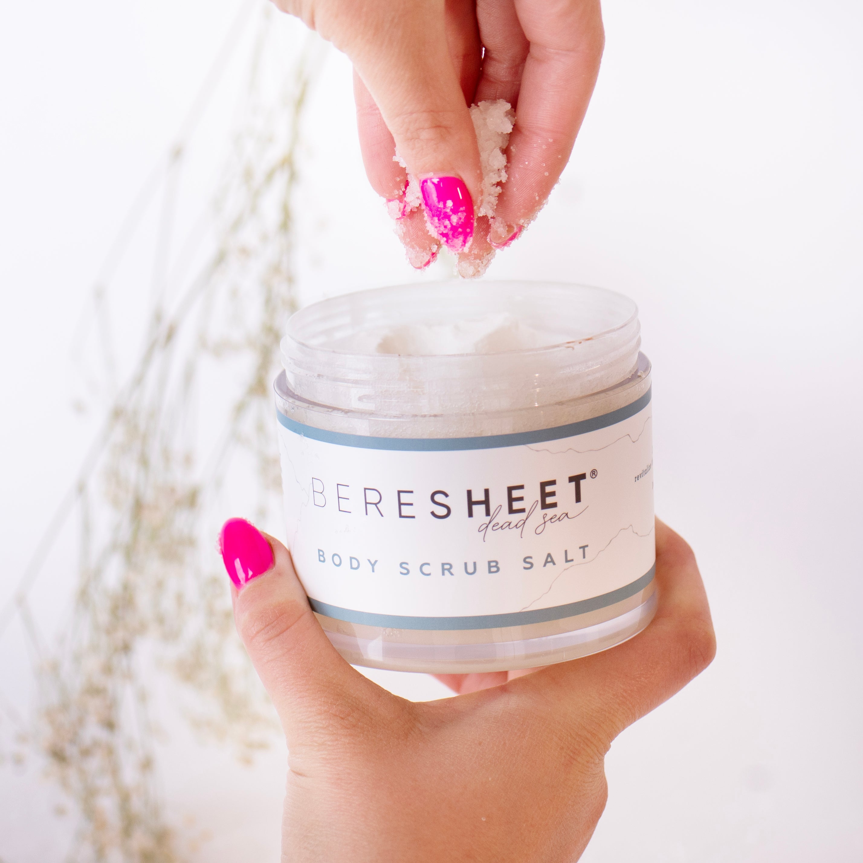 Hand holding a jar of Bereshet body scrub salt with a blurred background