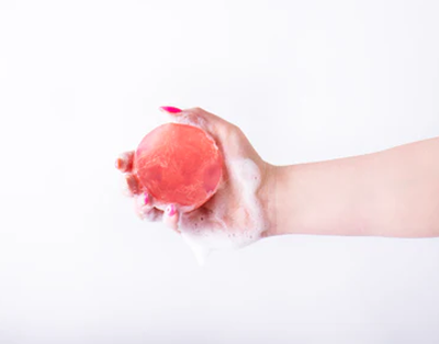 Hand holding a pink bath bomb against a white background