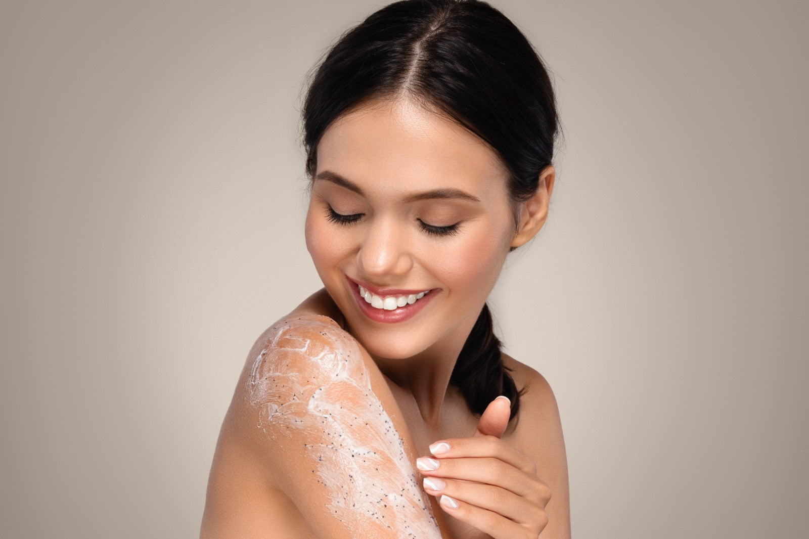 Woman applying cream to her arm against a neutral background