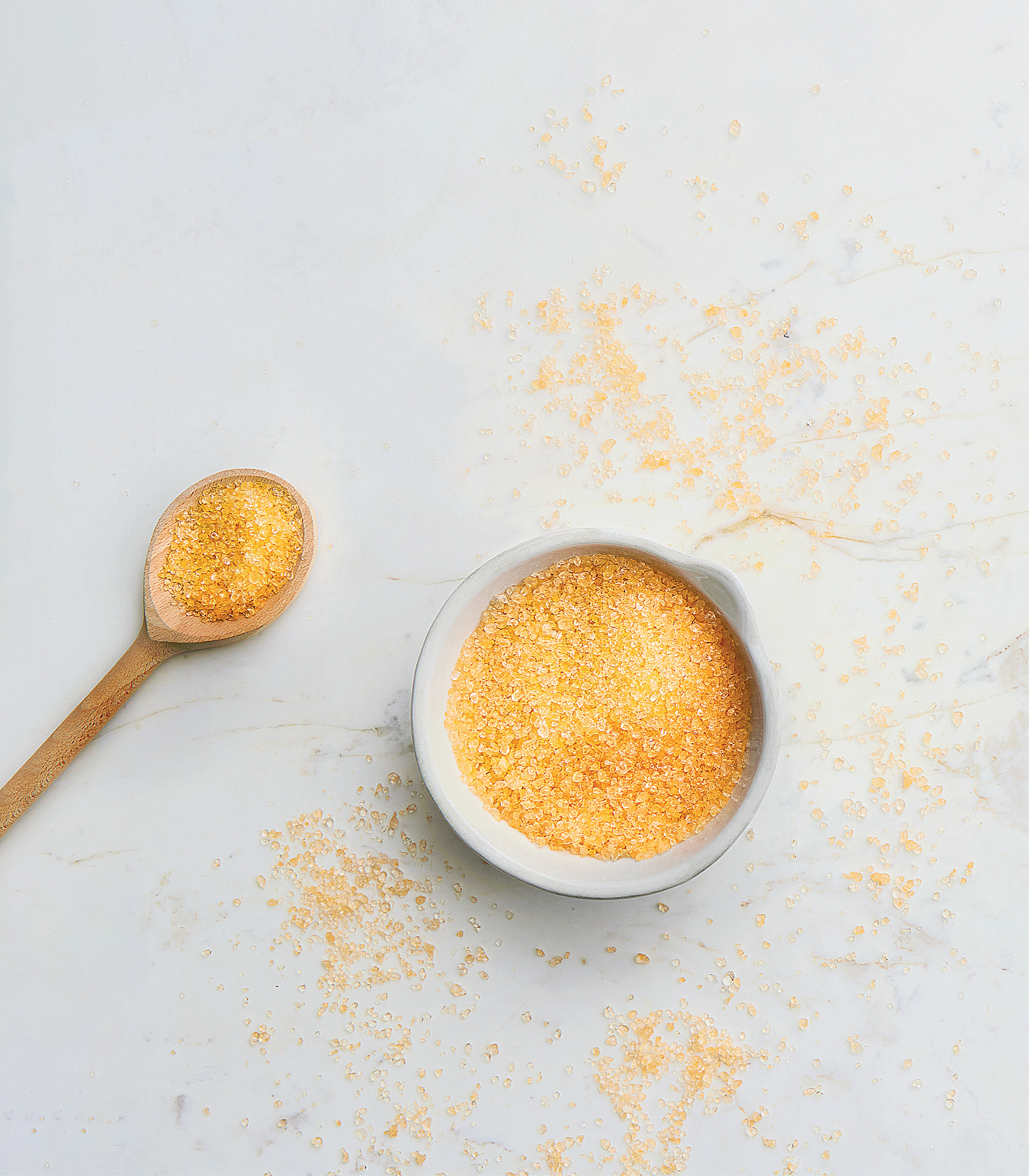 Small bowl and wooden spoon filled with yellow powder on a light gray surface