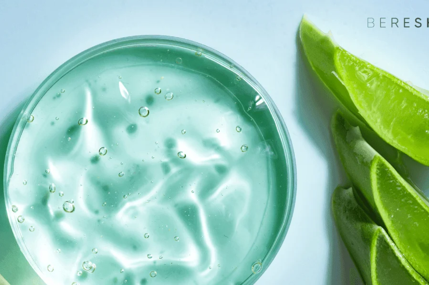 Green gel in a bowl with aloe vera leaves on a light blue background