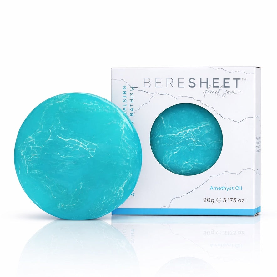 Turquoise bath bomb with marbled pattern next to its packaging on a white background