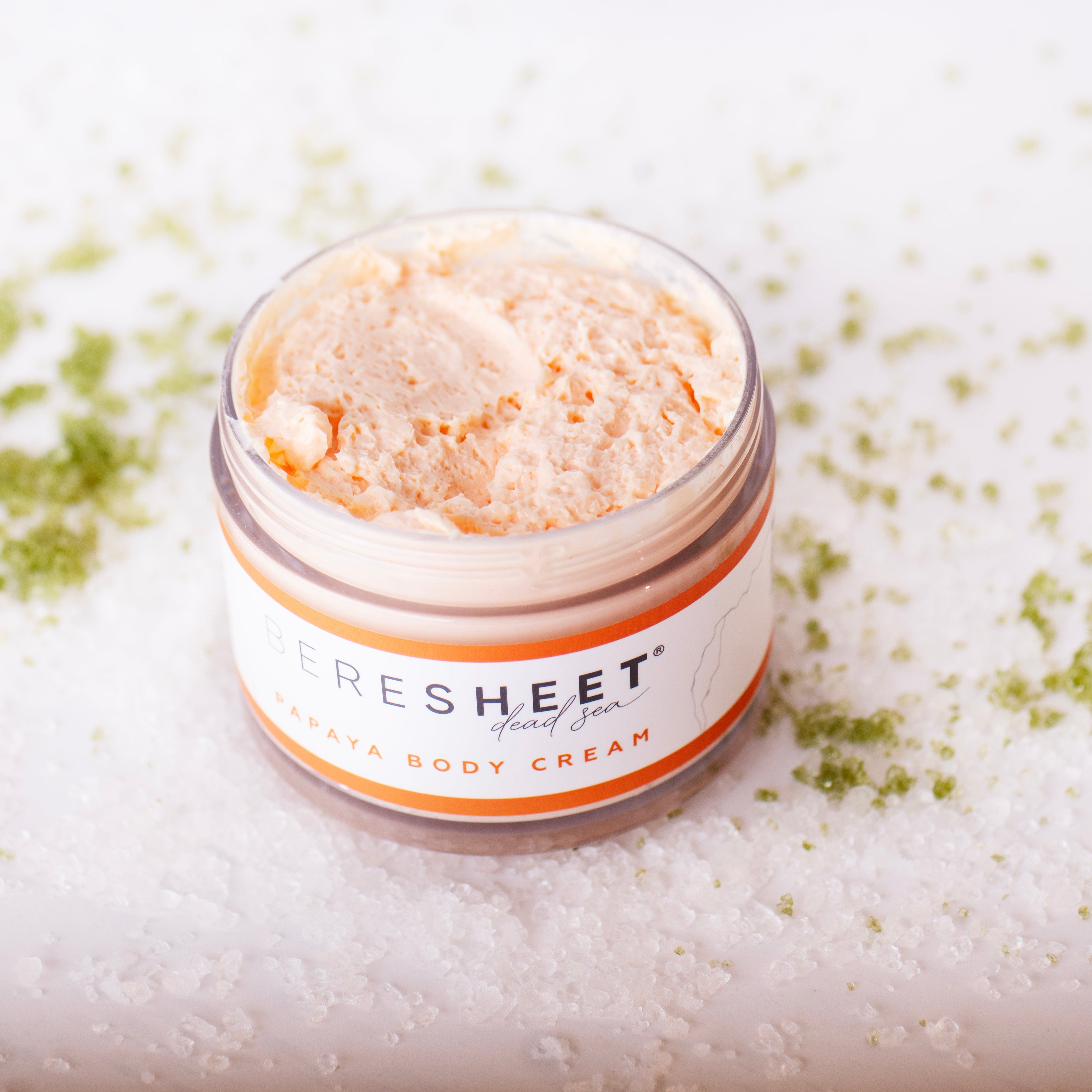 Jar of SRESHEET body cream on a textured white background with green powder.