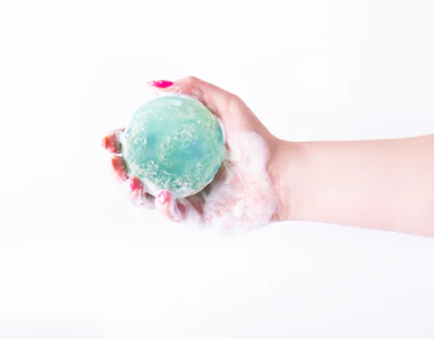 Hand holding a green bath bomb against a white background