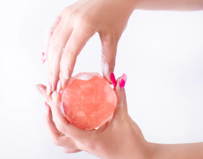 Close-up of hands holding a pink crystal ball against a white background