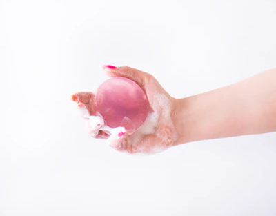 Hand holding a pink bath bomb with water droplets on a white background