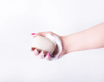 Hand holding a white bar of soap against a light background