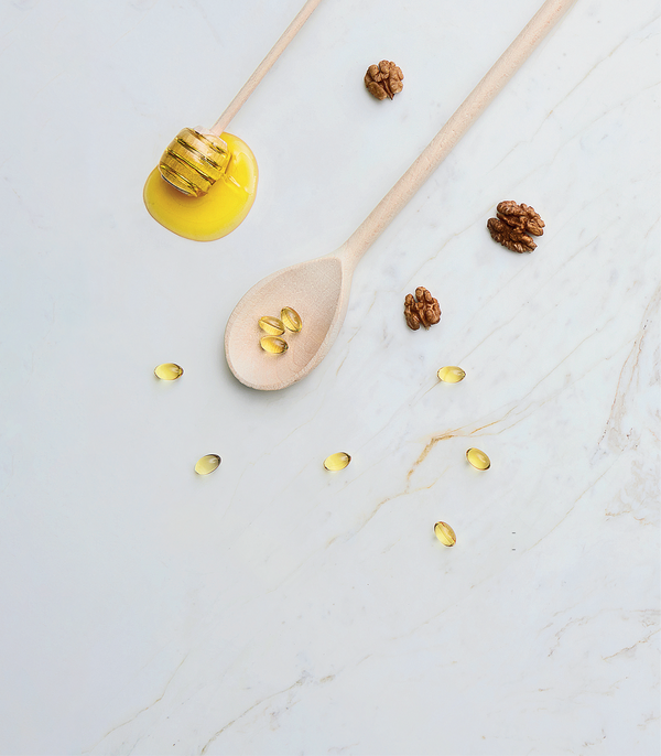 Wooden spoon with honey, walnuts, and capsules on a marble surface