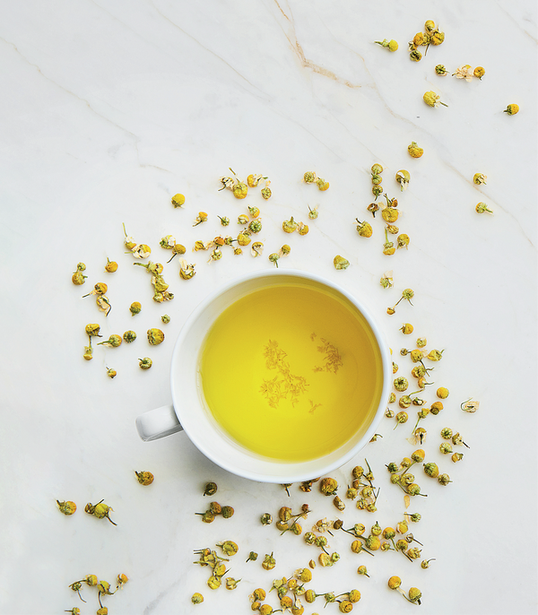 White cup of yellow tea with dried yellow flowers on a light surface