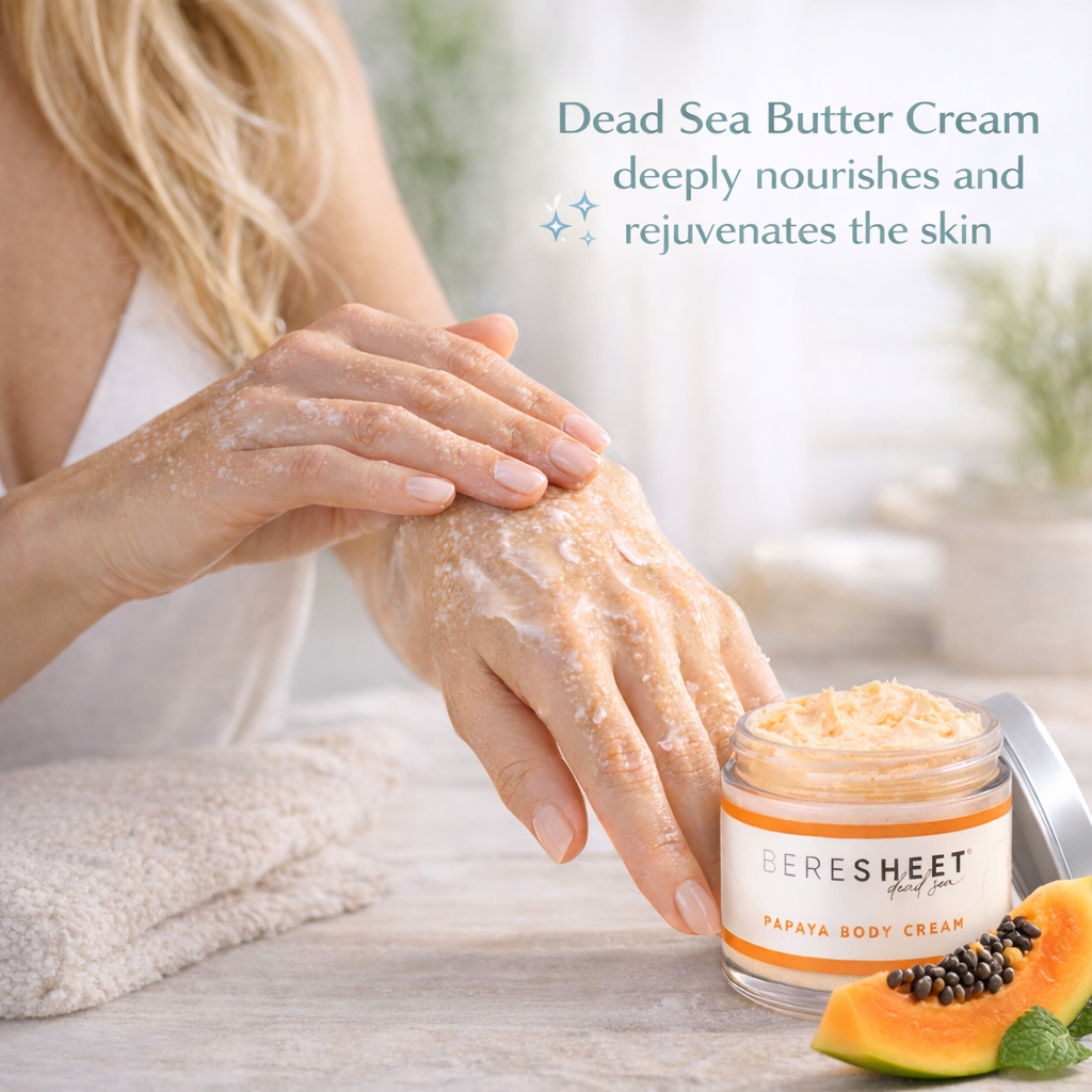 Person applying Dead Sea Butter Cream to their hand with a jar of the cream and papaya on a table.