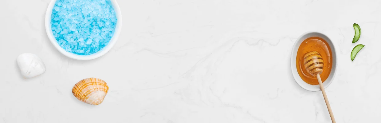 Honey dipper with honeycomb design, bowl of blue bath salts, and seashell on a light background